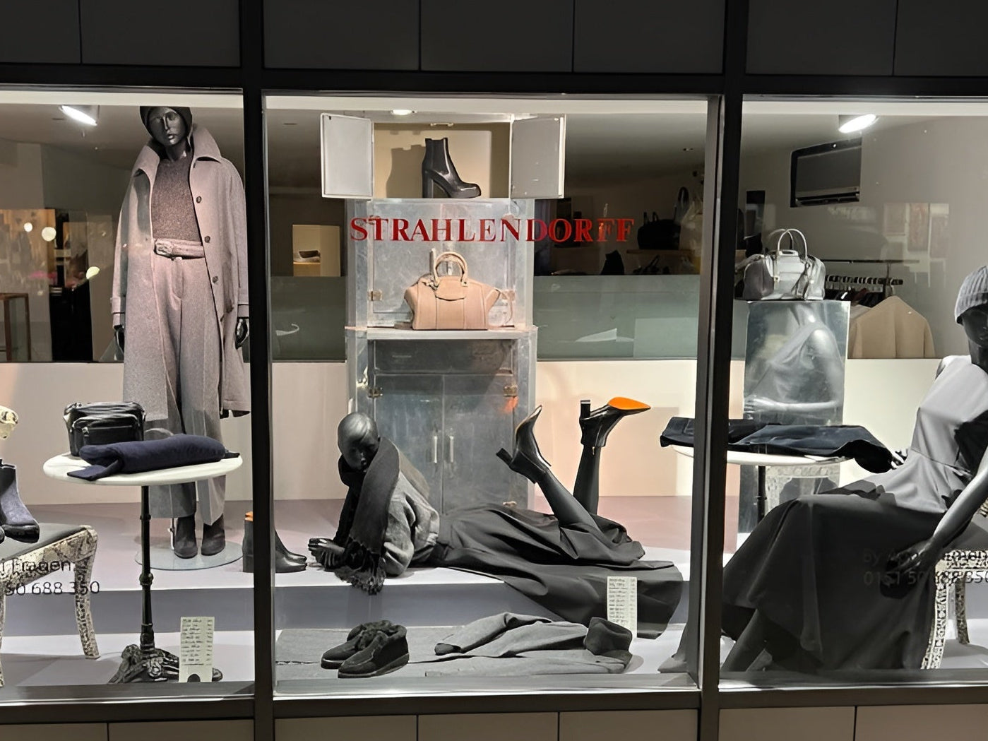 Schaufenster von Strahlendorff Hamburg mit luxuriöser Damenmode, Designer-Handtaschen und eleganter Boutique-Präsentation bei Nacht.